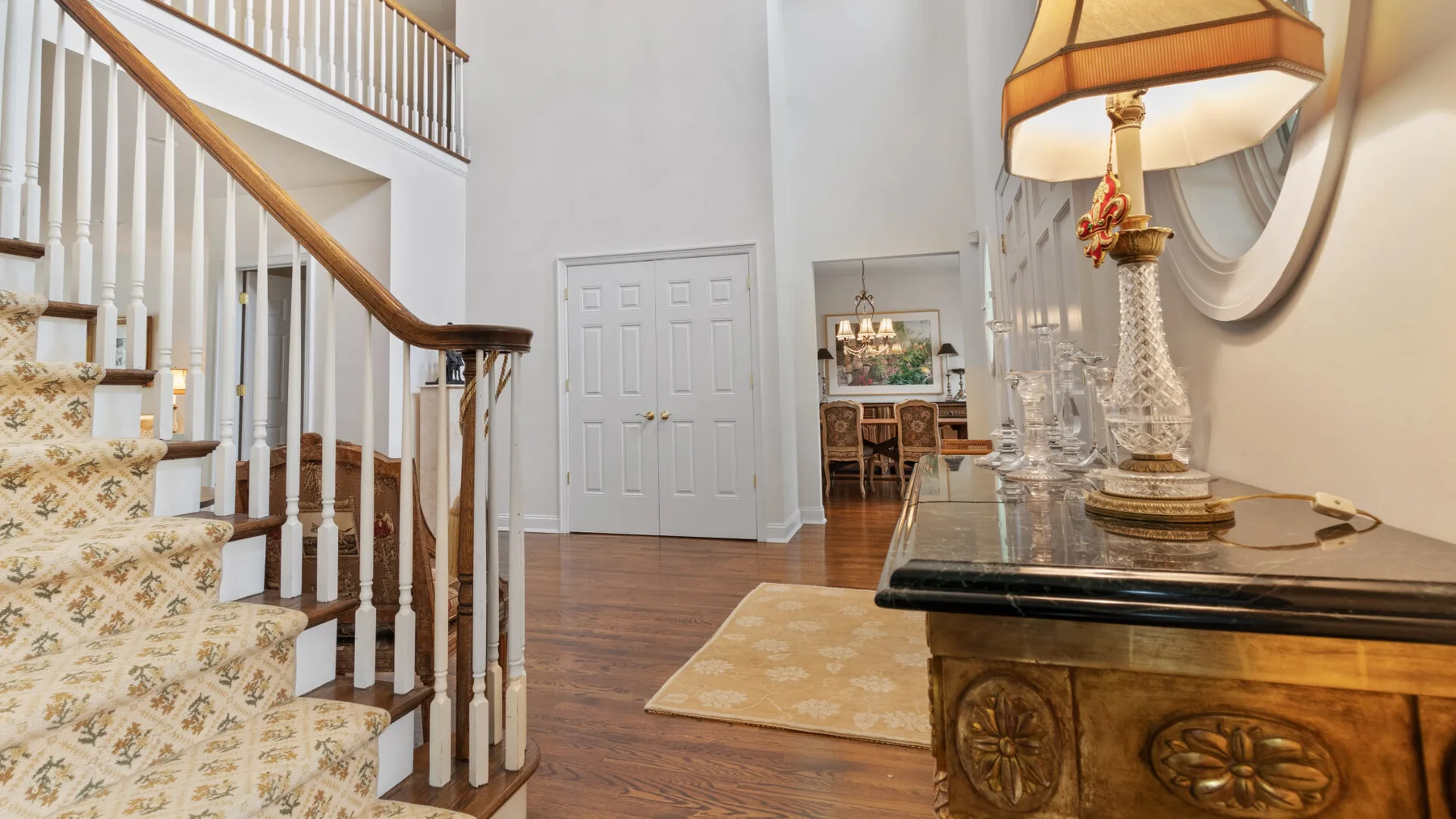 A bright interior hallway with a staircase, polished wood flooring, and a console table.