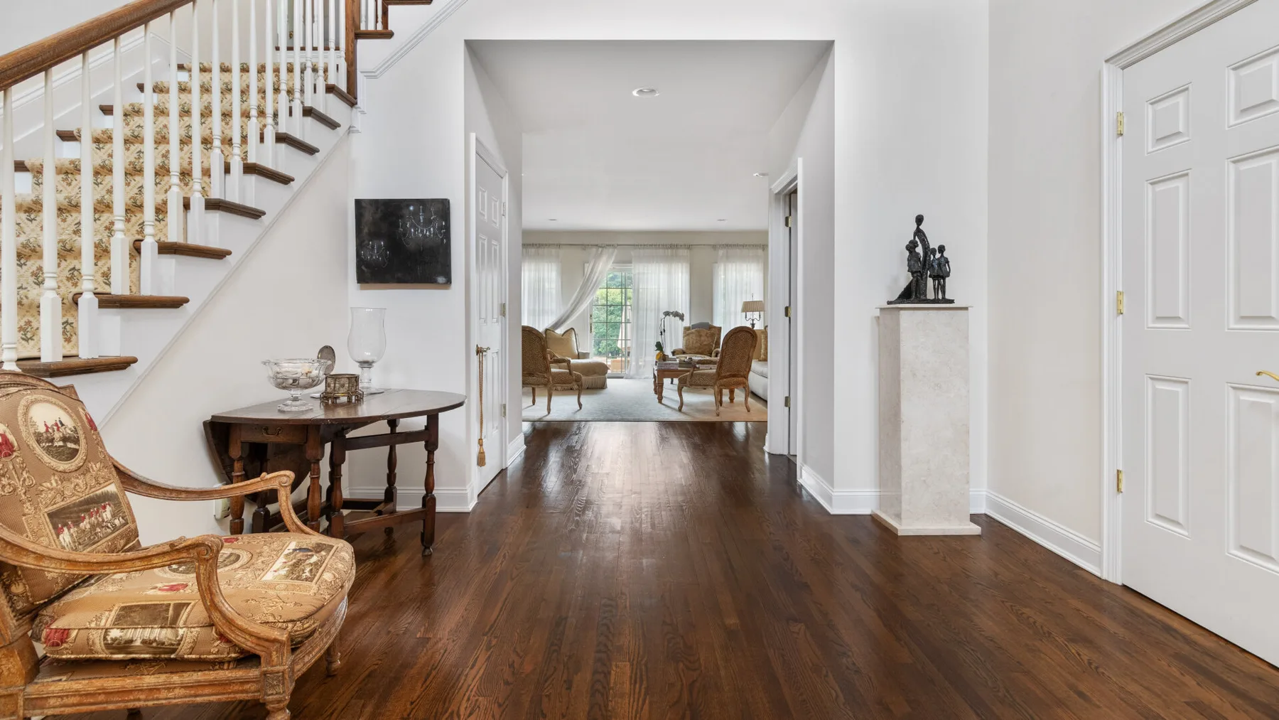 A bright home interior with a staircase and a hallway leading to a sitting area.
