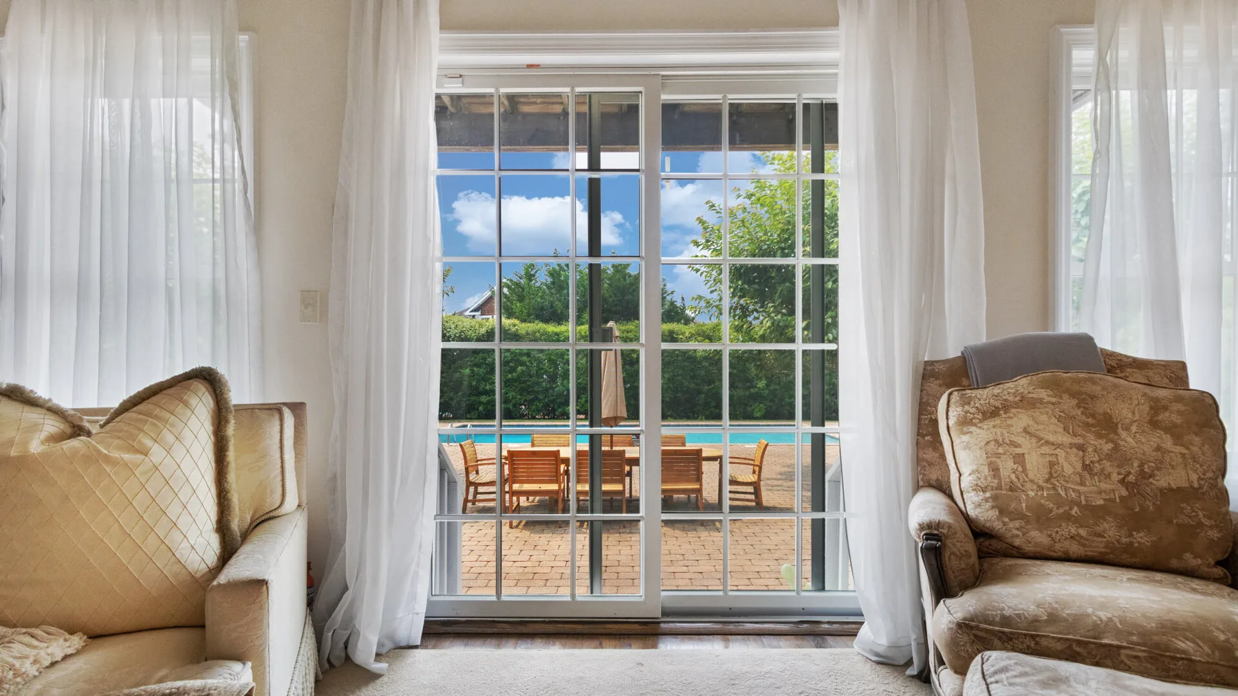 A bright living room with seating beside glass doors overlooking a patio and pool.