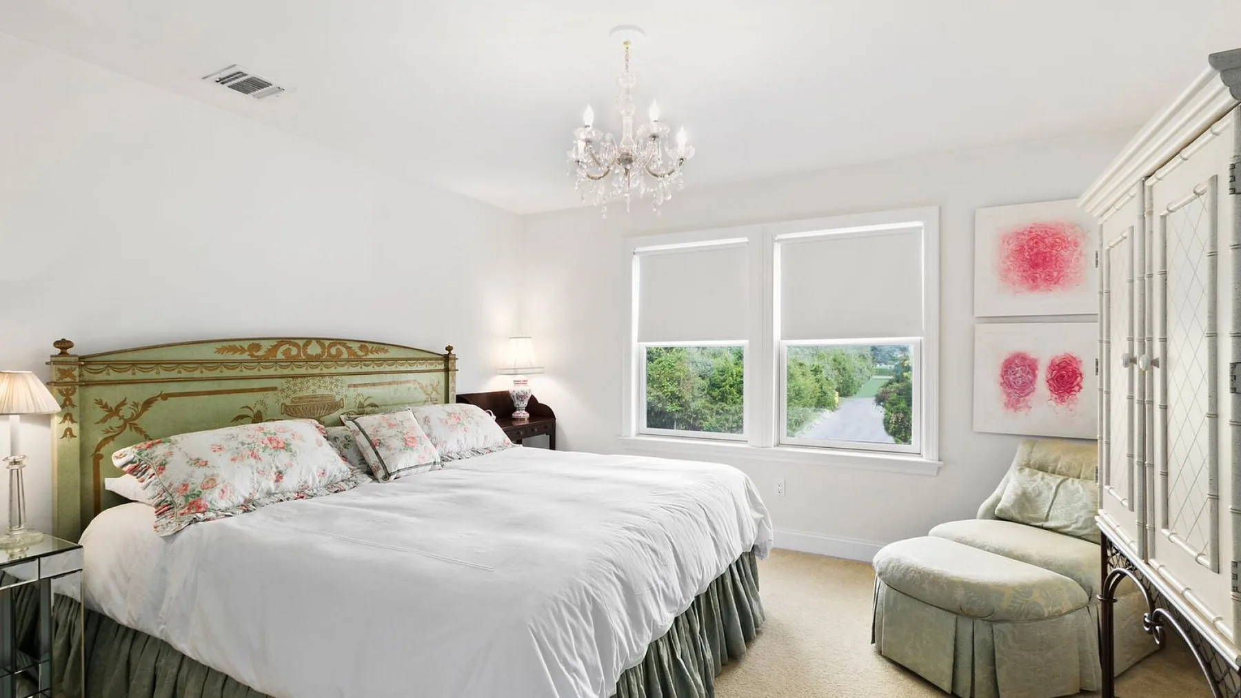 A bright bedroom with a large bed, two windows, and an upholstered seat.