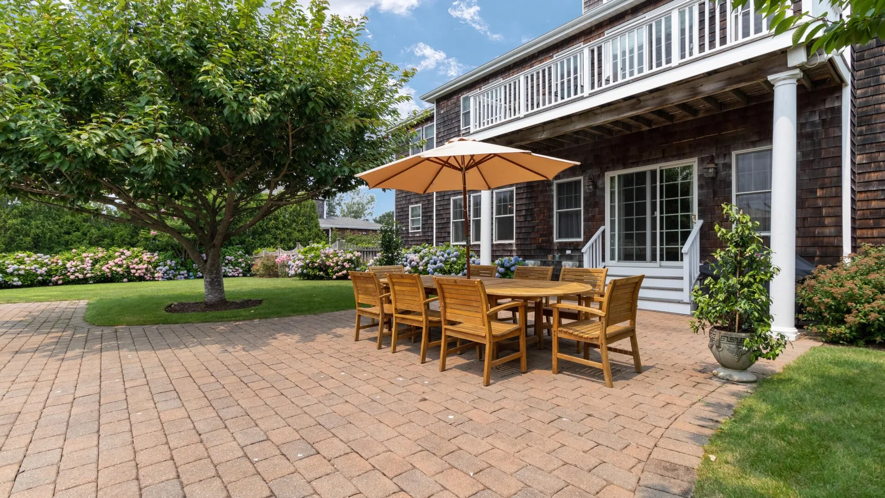 A brick patio beside a house has outdoor seating beneath a tan umbrella.