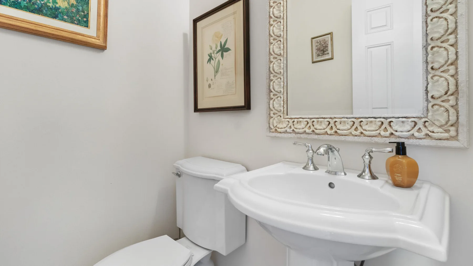 A bathroom sink sits beneath a large framed mirror, with framed artwork on the walls.