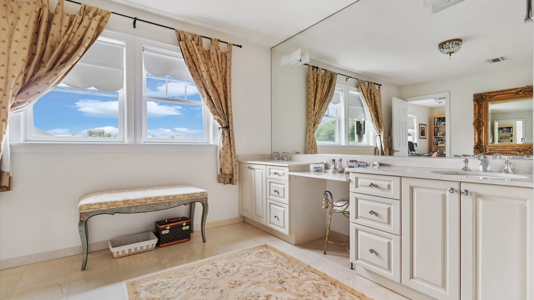 A bright bathroom with a long vanity, large mirror, and curtained windows.
