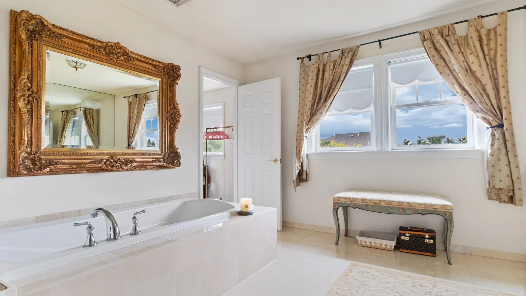 A bright bathroom with a built-in bathtub, large window, and decorative mirror.