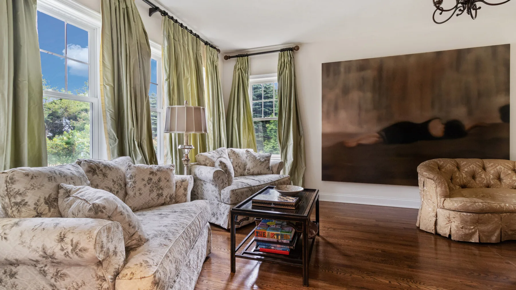 A living room with upholstered seating, a coffee table, and tall curtained windows.