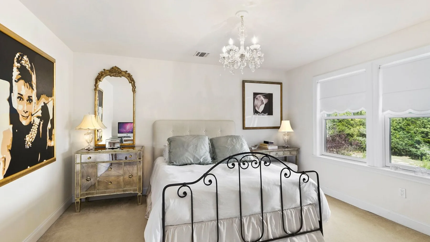 A bright bedroom with a bed, framed artwork, and two windows.