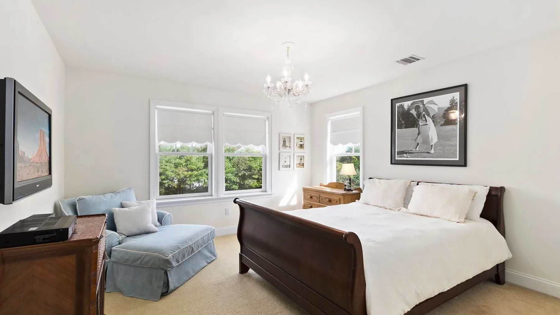 A bright bedroom with a large bed, a blue seat, and windows.