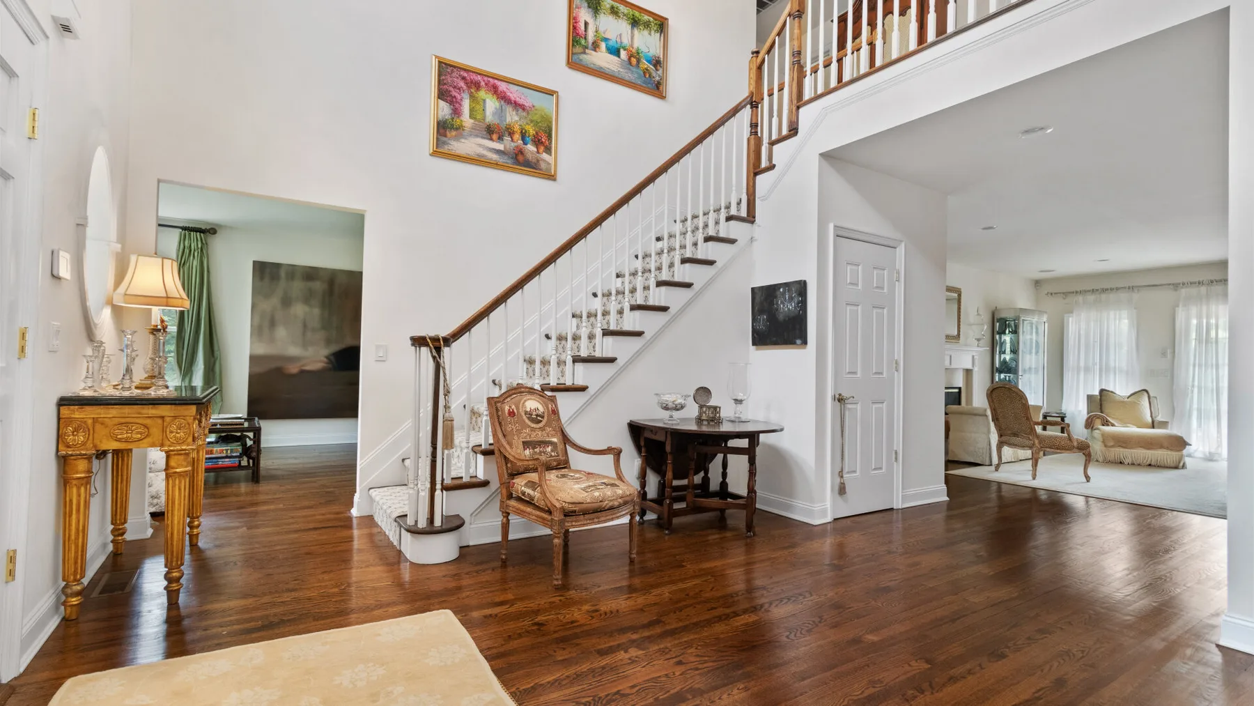 A bright living area with a staircase, polished wood flooring, and seating.