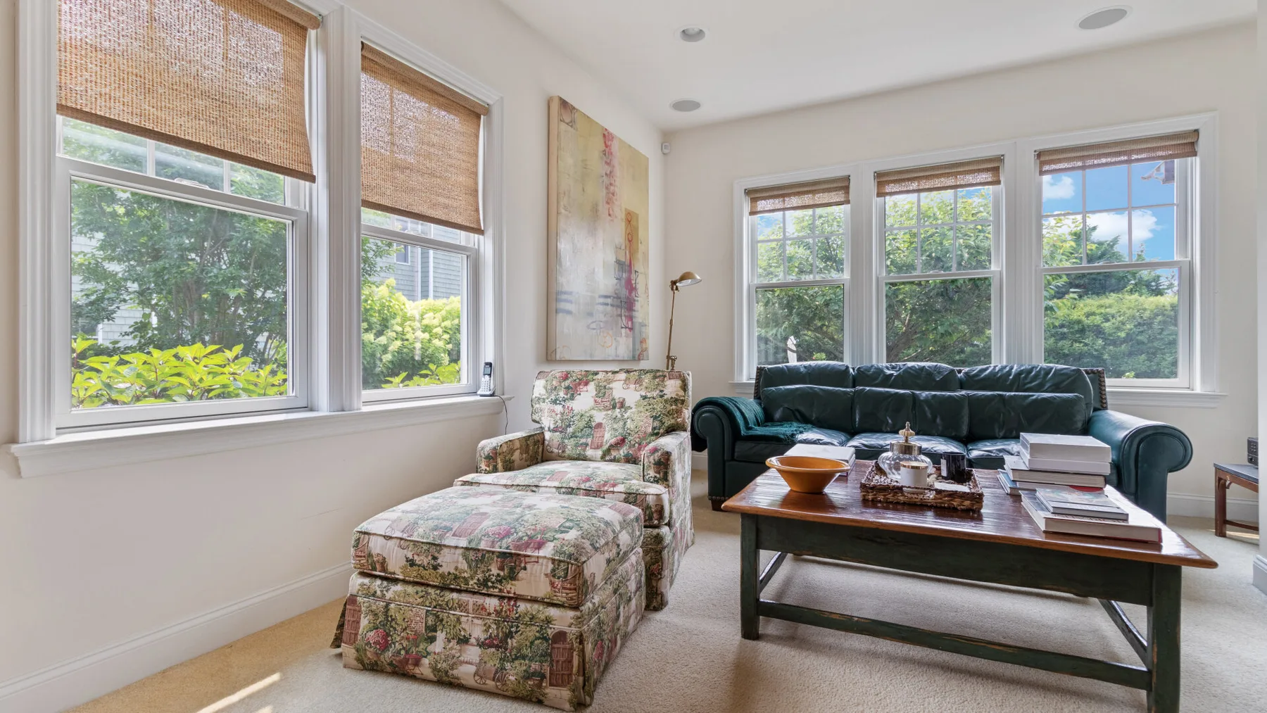 A bright living room with a dark sofa, floral seating, and large windows.