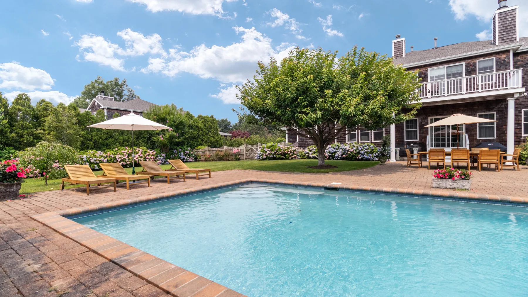 An outdoor swimming pool beside a landscaped patio and a large house.