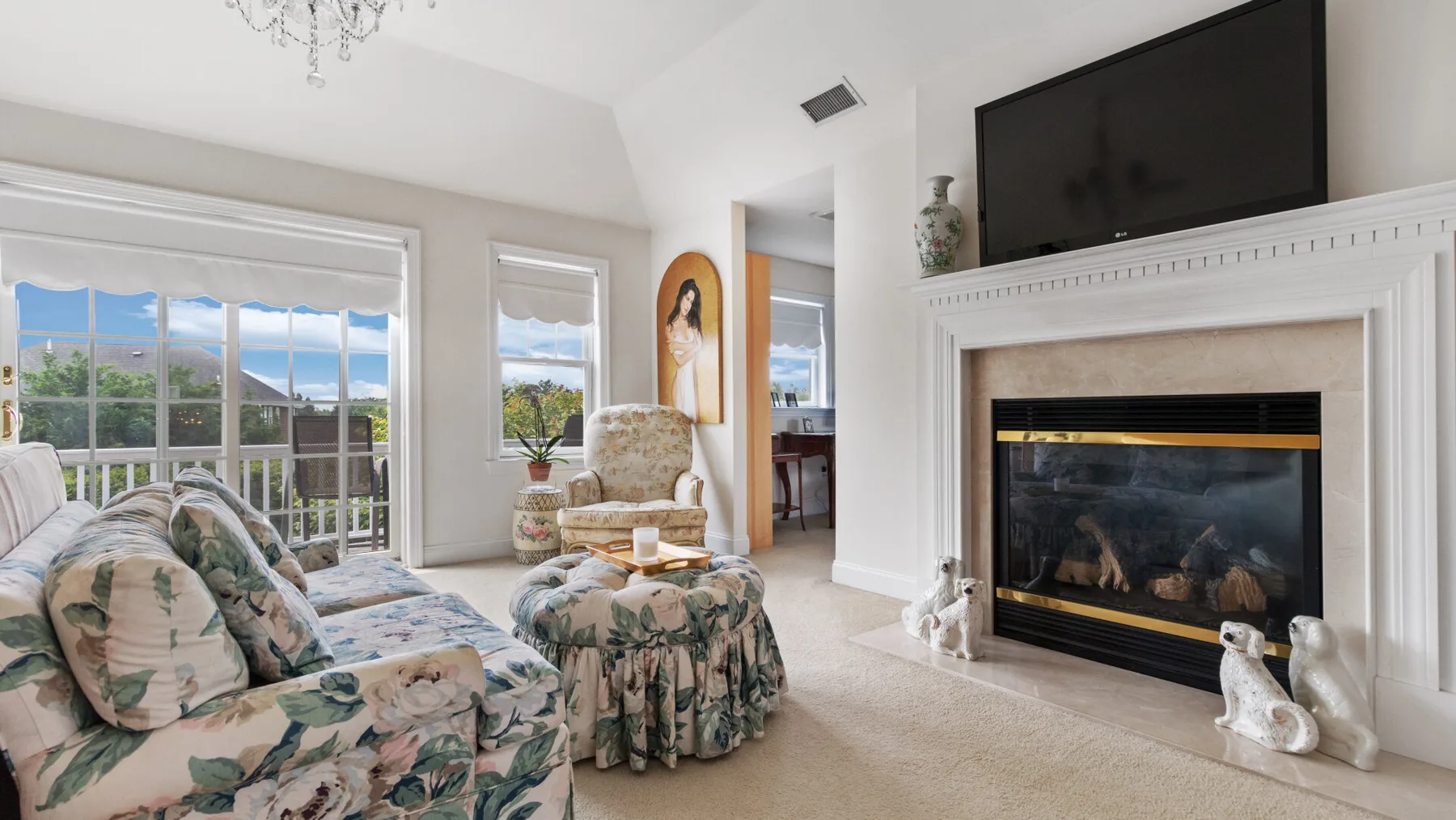 A living room with floral seating, large windows, and a fireplace.