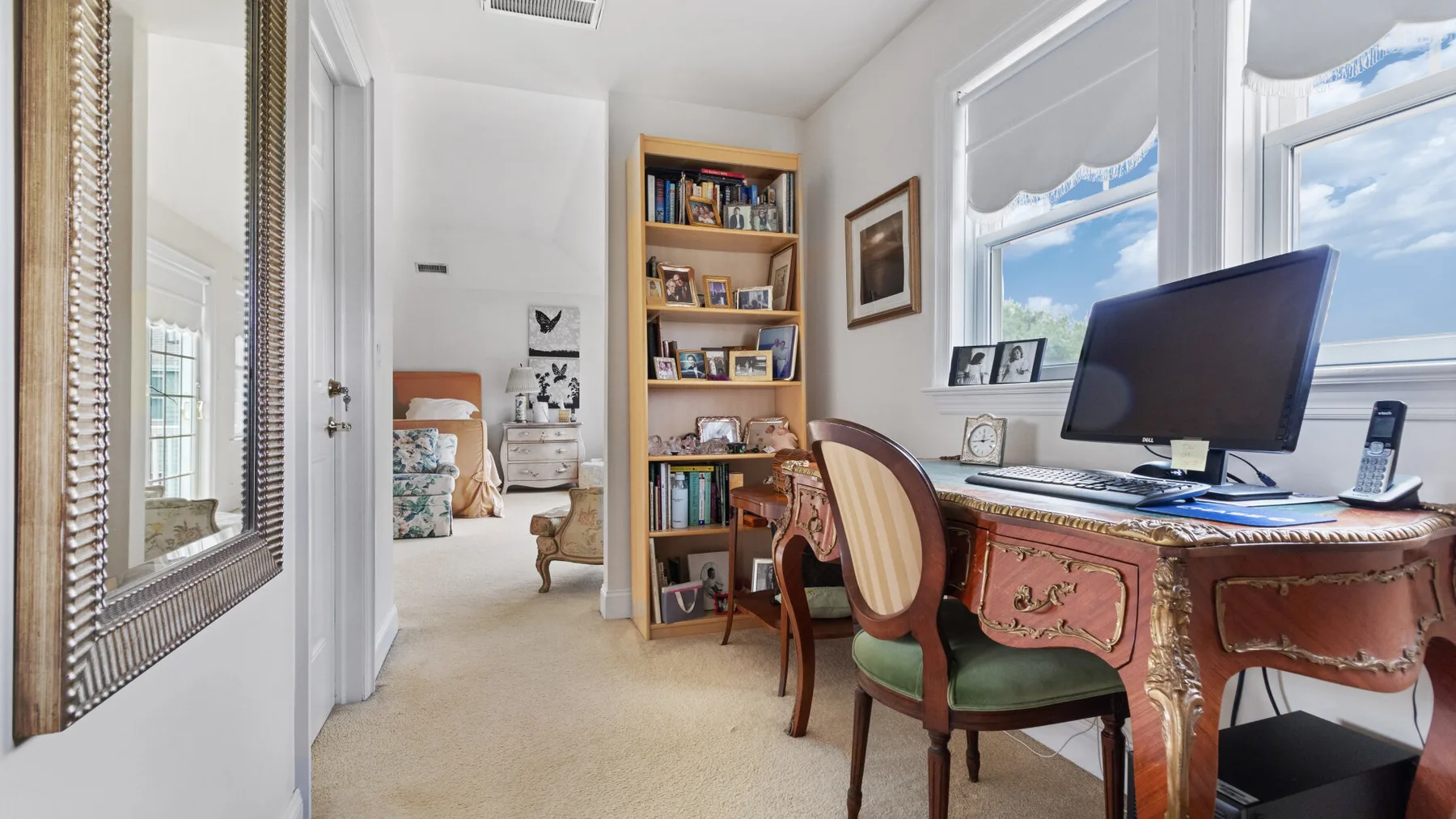 A study with a desk, computer, and bookshelves beside bright windows.