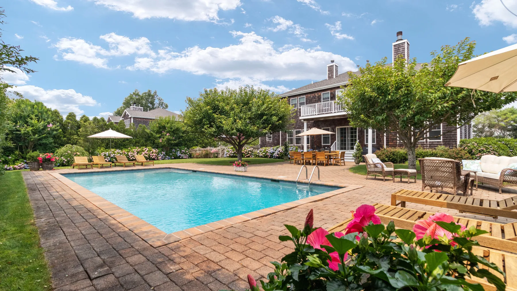 An outdoor swimming pool beside a patio with seating and flowering plants.
