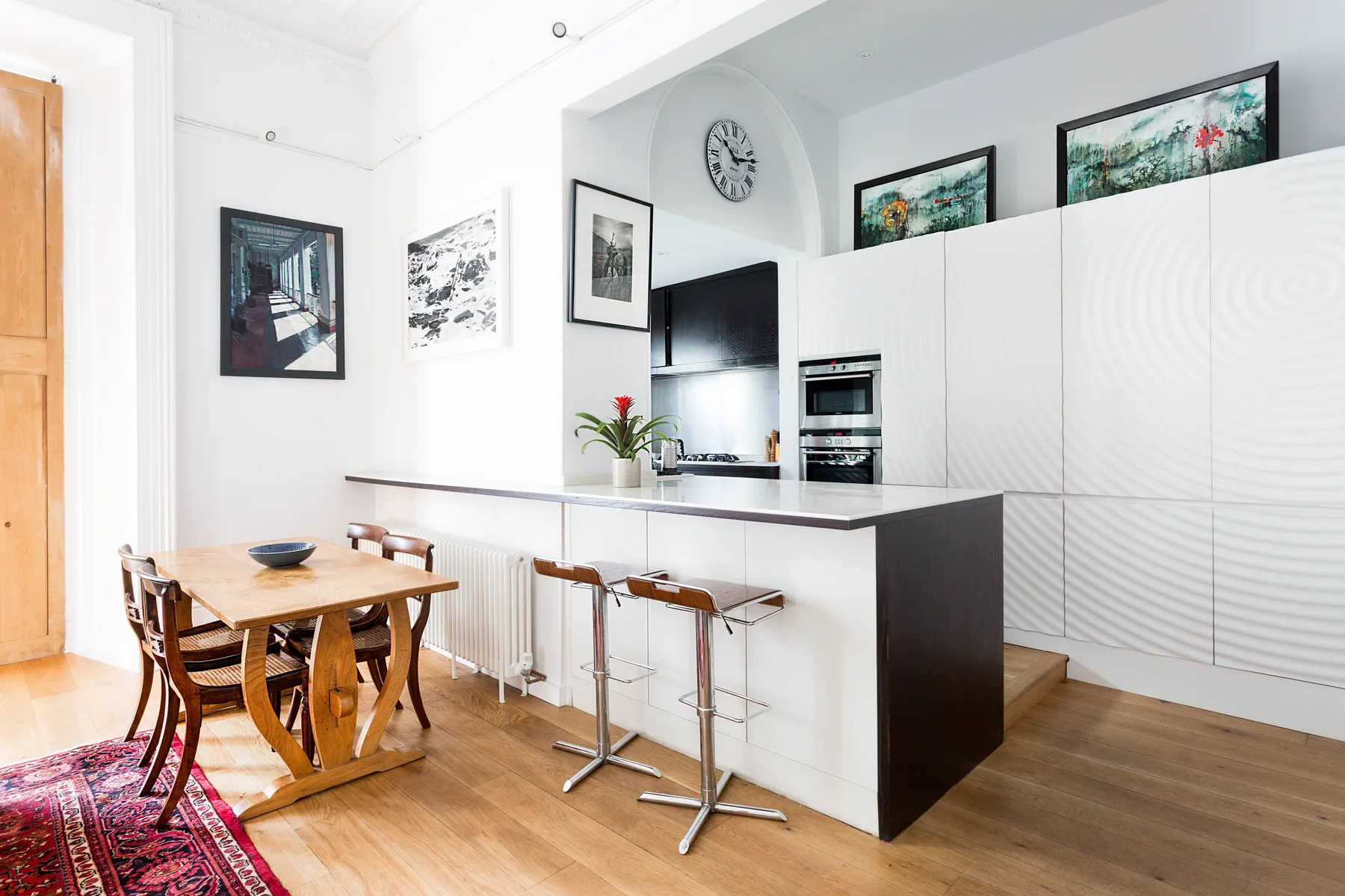 A bright kitchen and dining area with a counter, bar seating, and a wooden table.