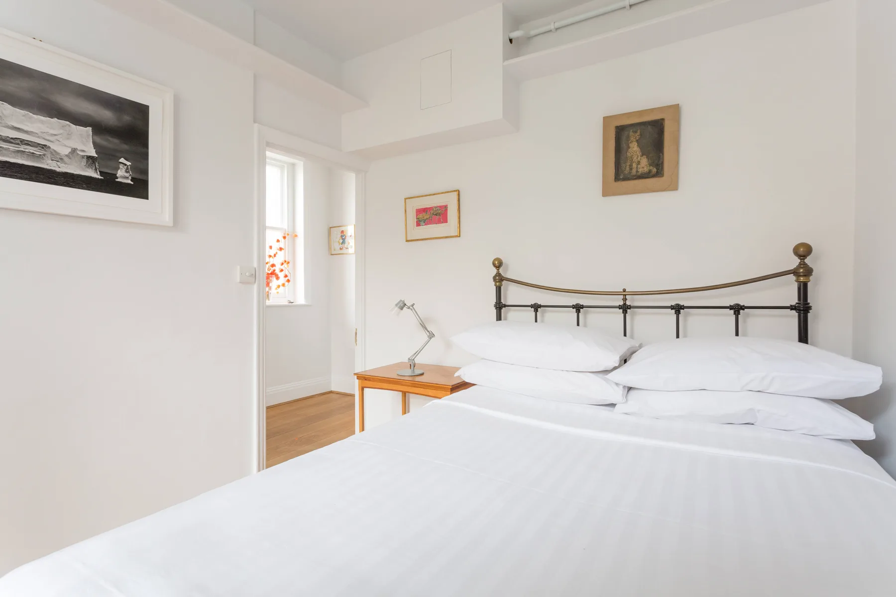 Un dormitorio luminoso con una cama bien tendida y cuadros en las paredes.
