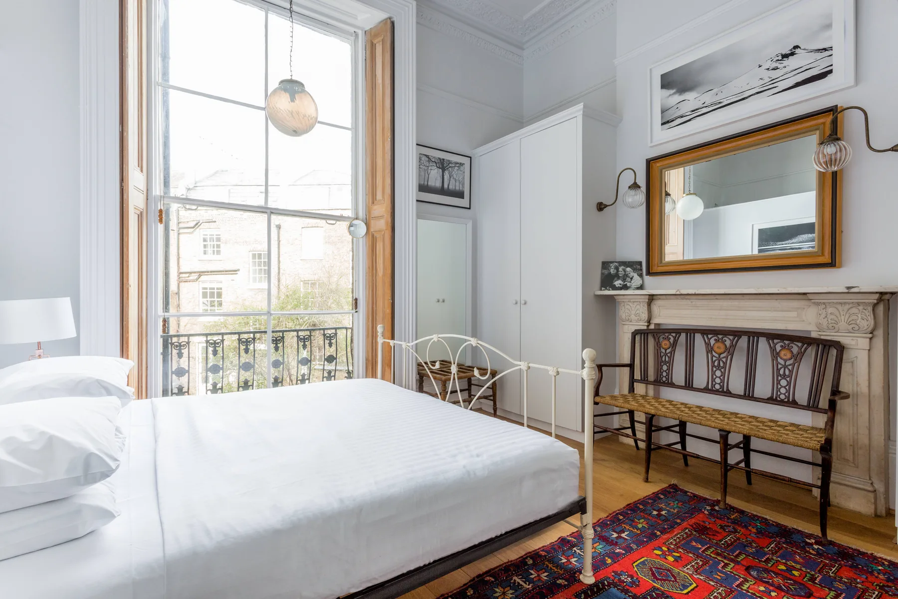Un dormitorio luminoso con una cama grande junto a una ventana alta y una alfombra estampada.