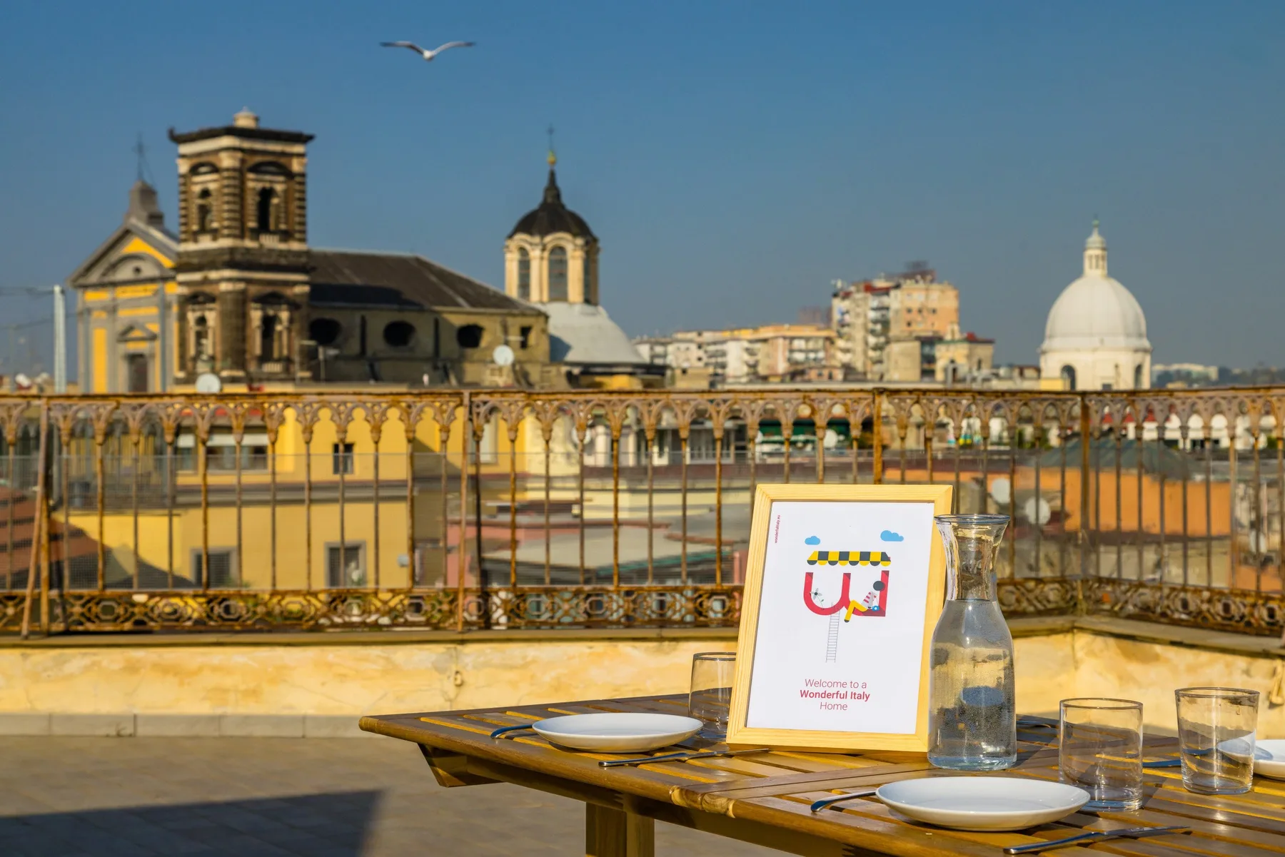 A rooftop dining table overlooks historic city buildings beneath a clear blue sky.