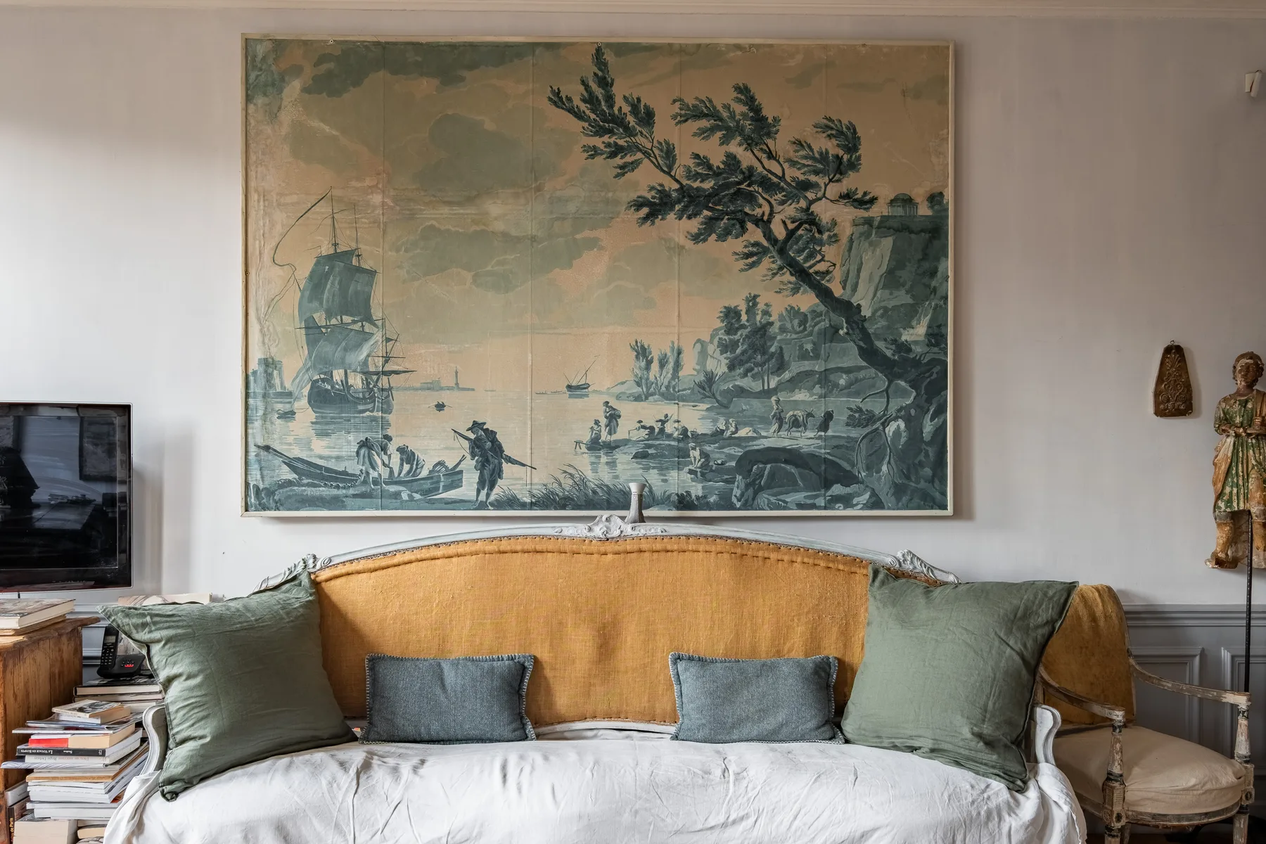 A bed with green pillows sits beneath a large framed landscape artwork.