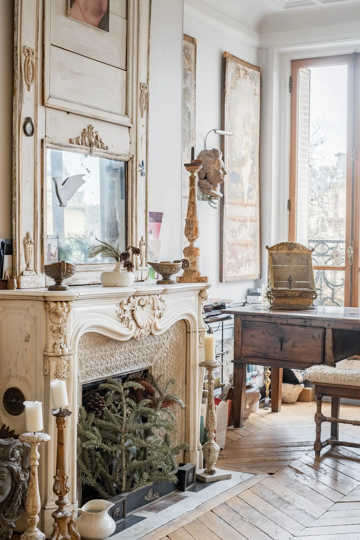 A bright living room with an ornate fireplace and a wooden desk by the window.