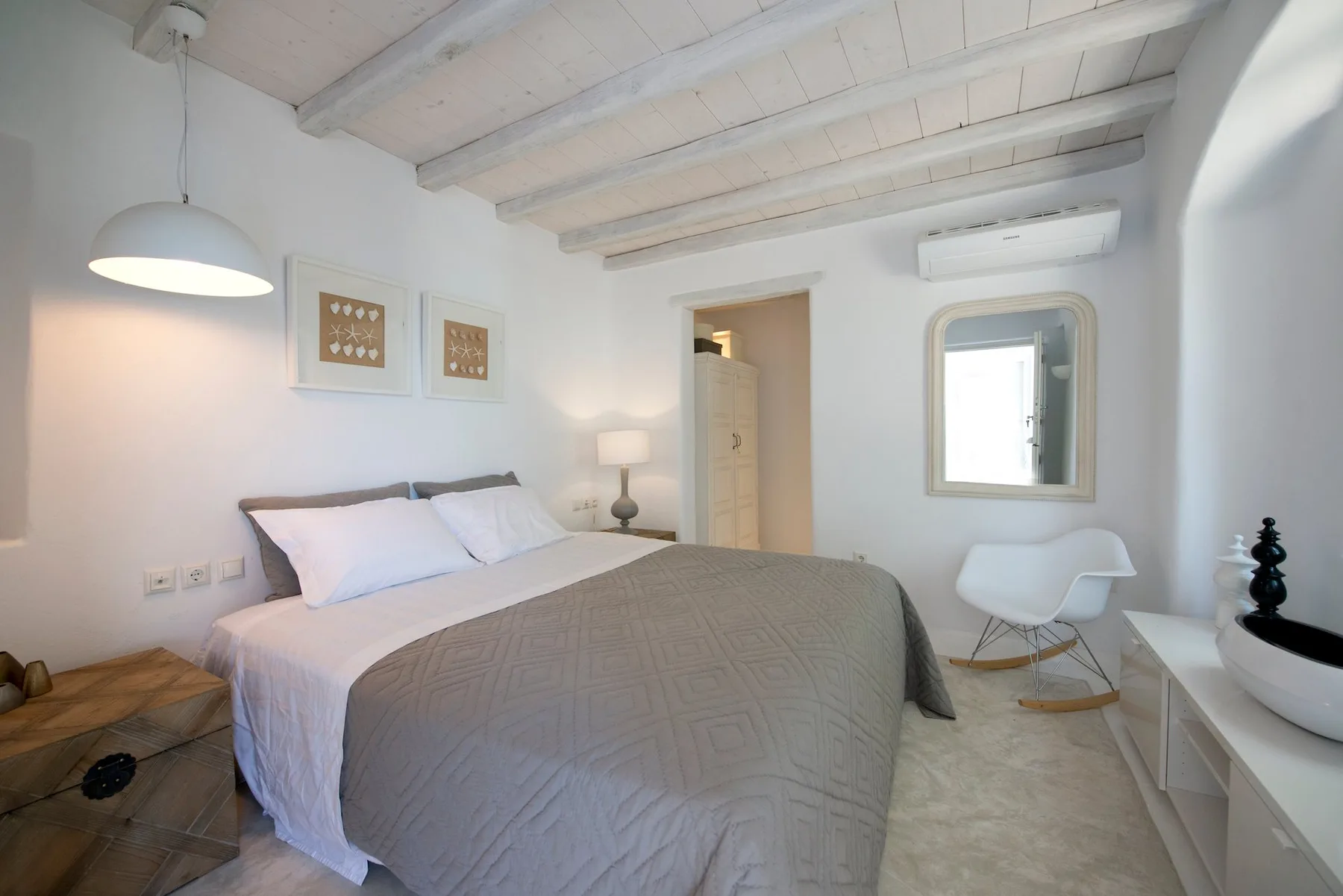 A bright bedroom with a neatly made bed, wall art, and a chair by the window.