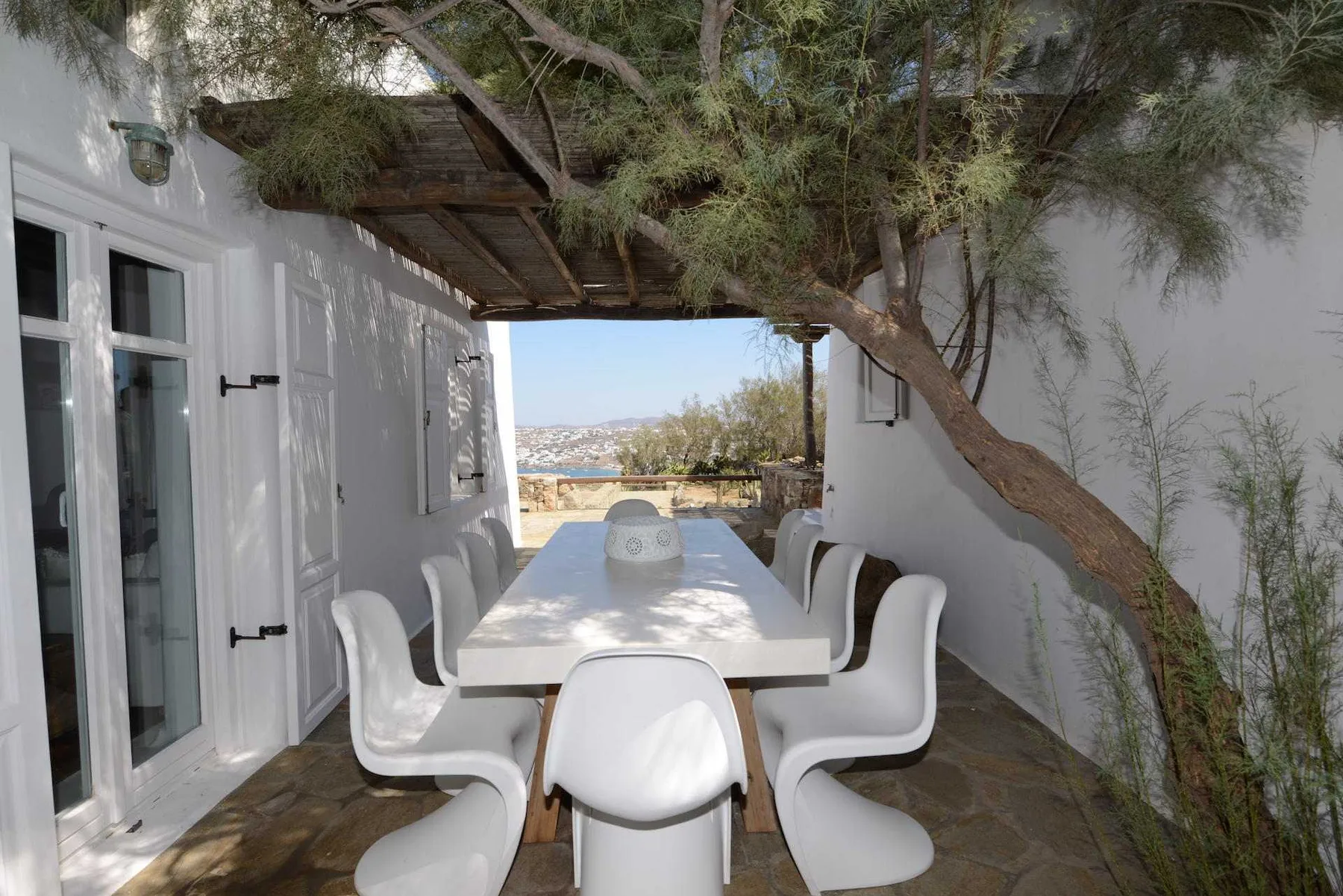 An outdoor dining area has a long table beneath a tree.