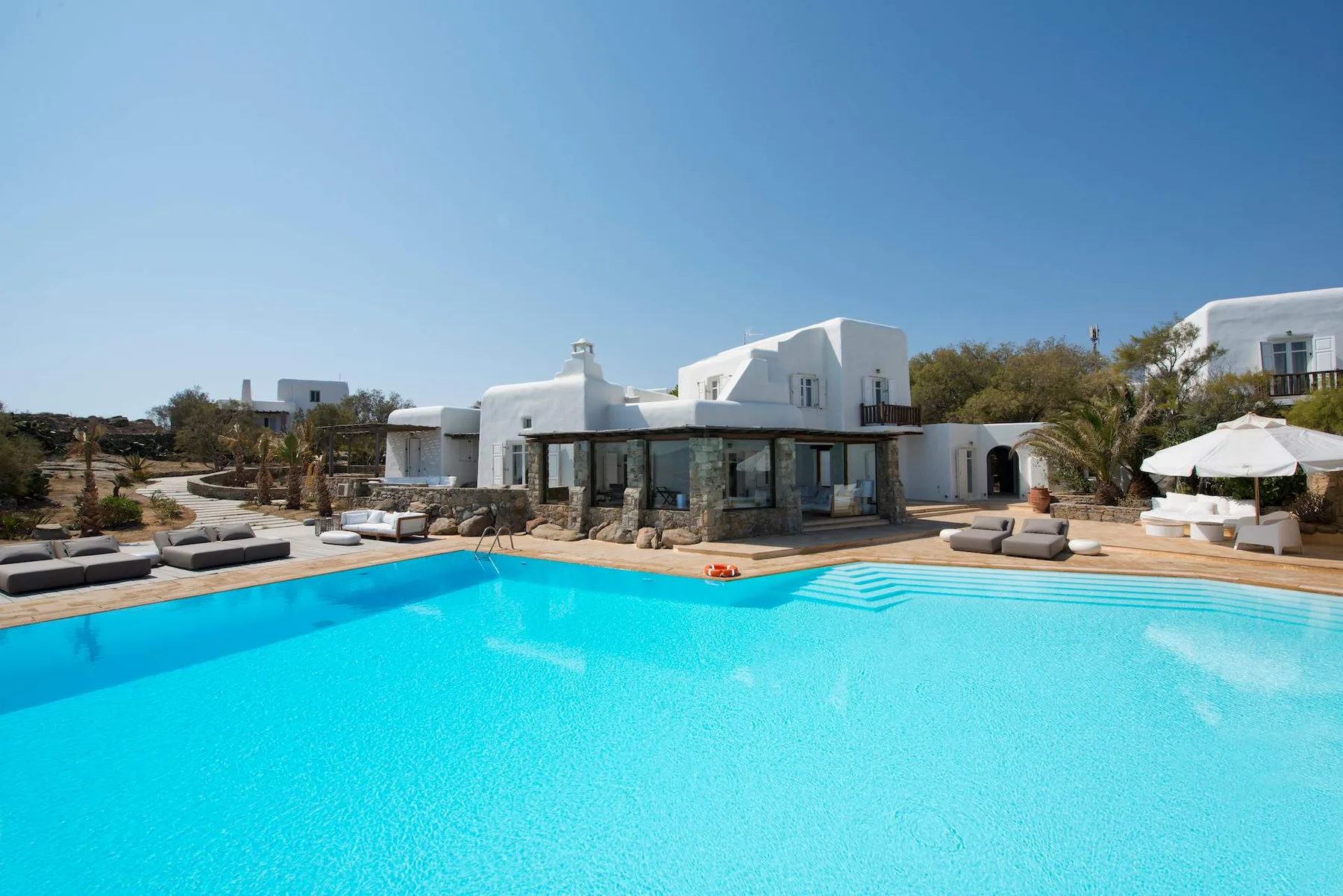 A swimming pool in front of white buildings, with lounge seating along the deck.