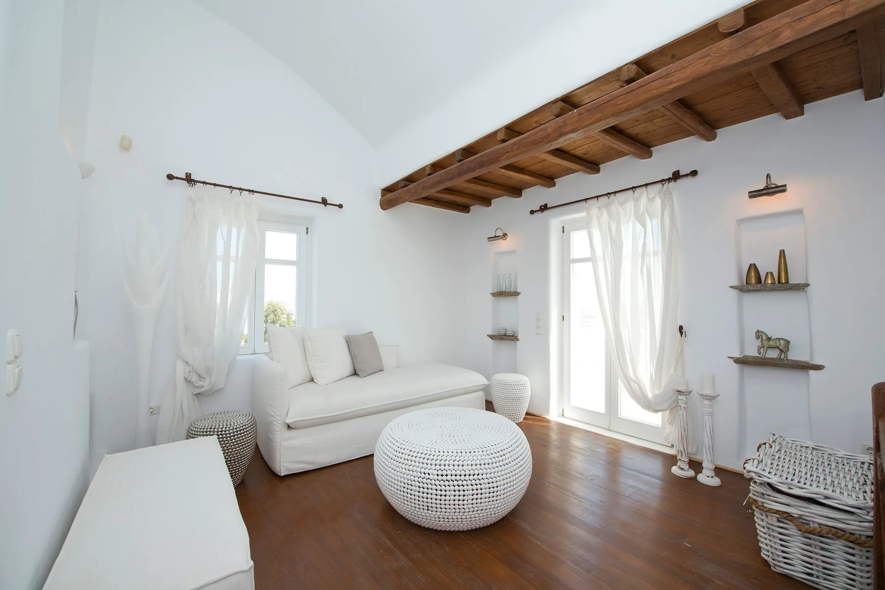 A bright living room with white seating beneath exposed wooden ceiling beams.