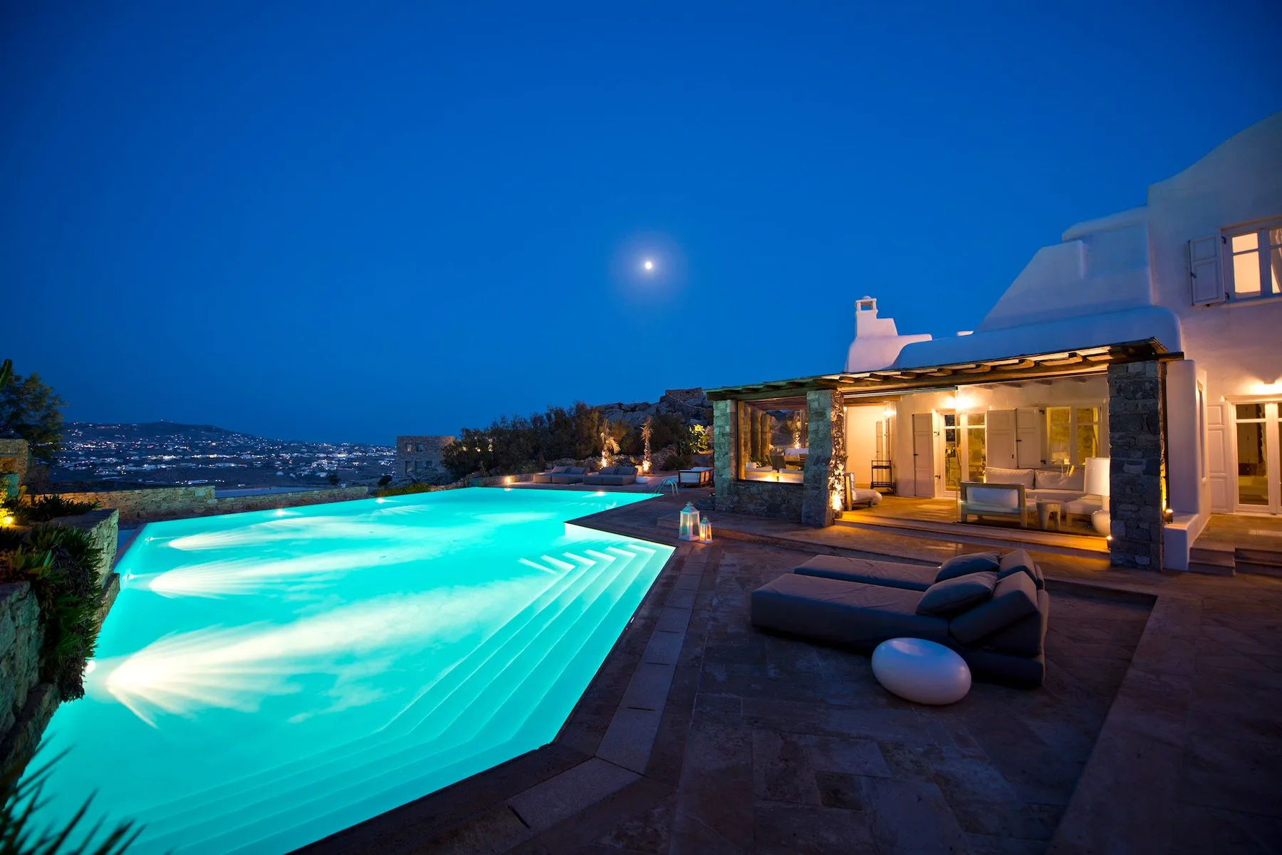 An illuminated outdoor pool beside a modern house at dusk.