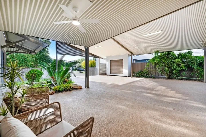 Un patio exterior cubierto con asientos, plantas de jardín y un ventilador de techo.