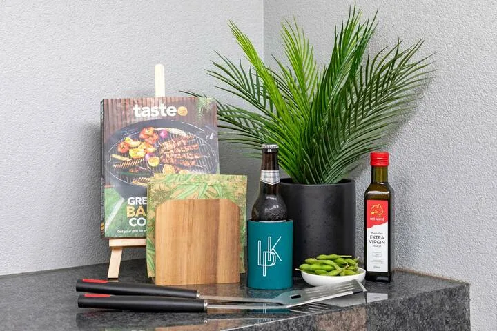 Una encimera de cocina muestra un libro de cocina, una tabla, aceite y una palmera en maceta.