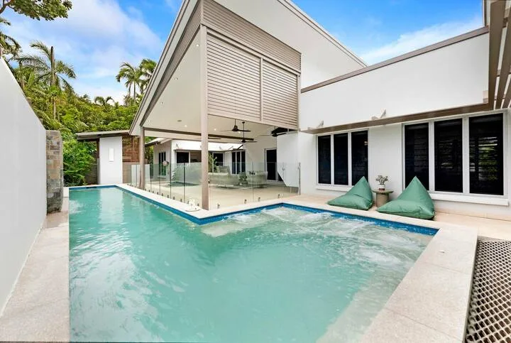 Una casa moderna rodea una piscina turquesa con una zona de spa elevada.