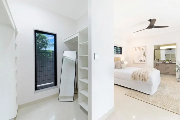 Un dormitorio luminoso con una cama, un ventilador de techo y un armario abierto.