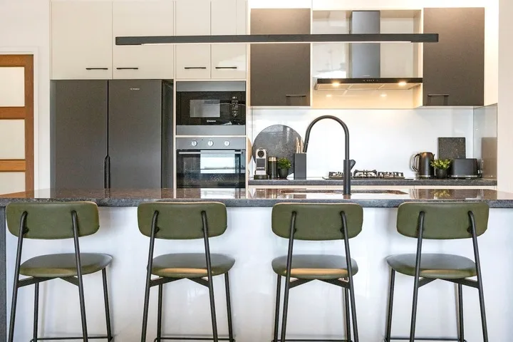 Una cocina moderna con una barra larga y cuatro taburetes verdes.