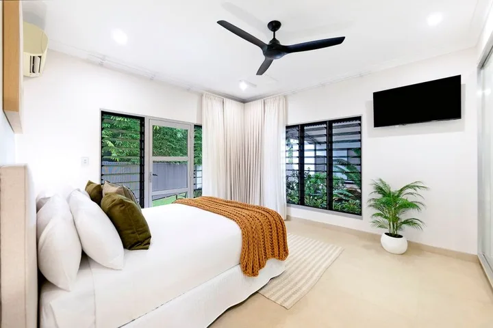 Un dormitorio luminoso con una cama bien hecha y ventanas con vistas a la vegetación.