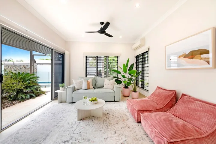 Una sala luminosa con asientos claros, sillones rosados y ventanas grandes.