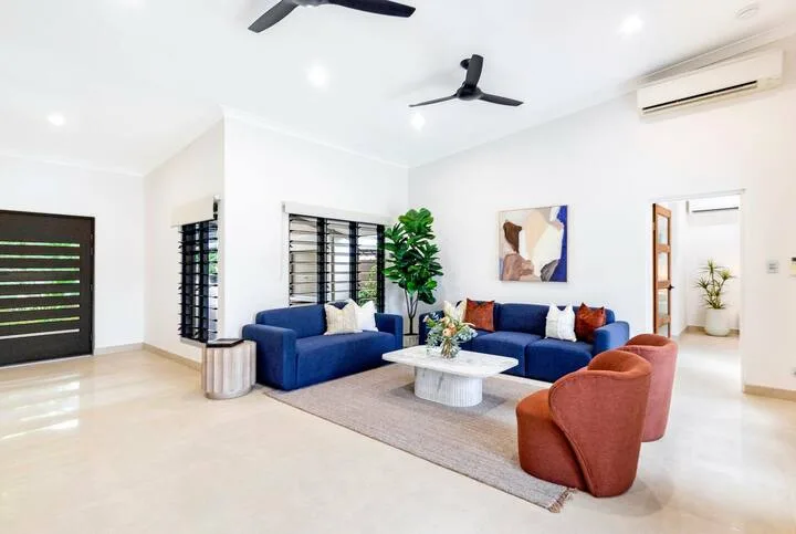 Una sala luminosa tiene asientos azules, una mesa de centro y ventiladores de techo.