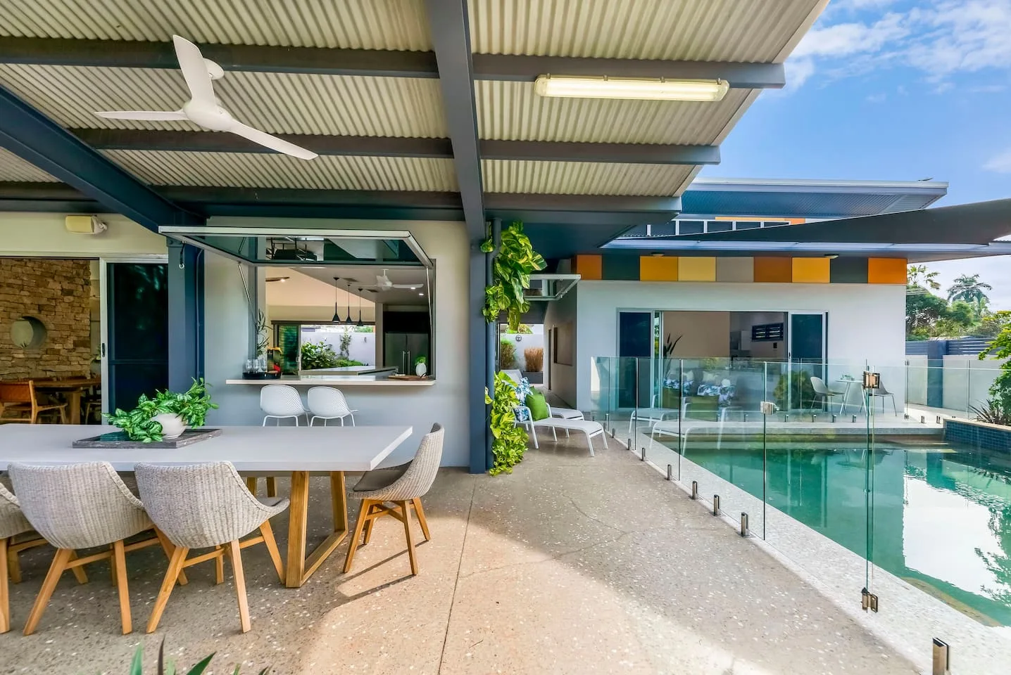 A covered outdoor dining area with a serving window overlooks a swimming pool.