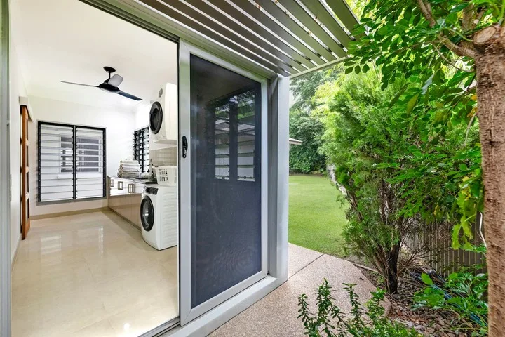 Una puerta corrediza de vidrio da a un sendero ajardinado desde una luminosa zona de lavandería.