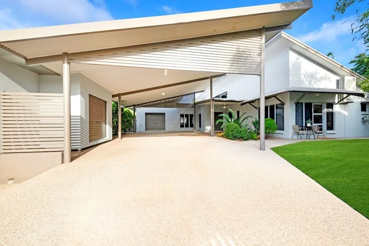 Una casa blanca moderna con una amplia entrada techada y césped verde.