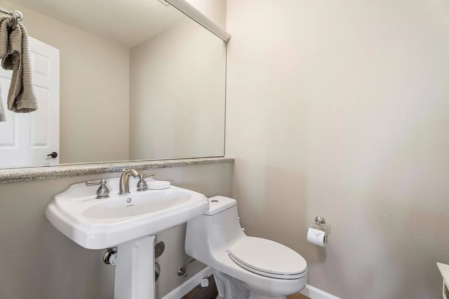 Un baño con lavabo de pedestal, inodoro y un gran espejo de pared.