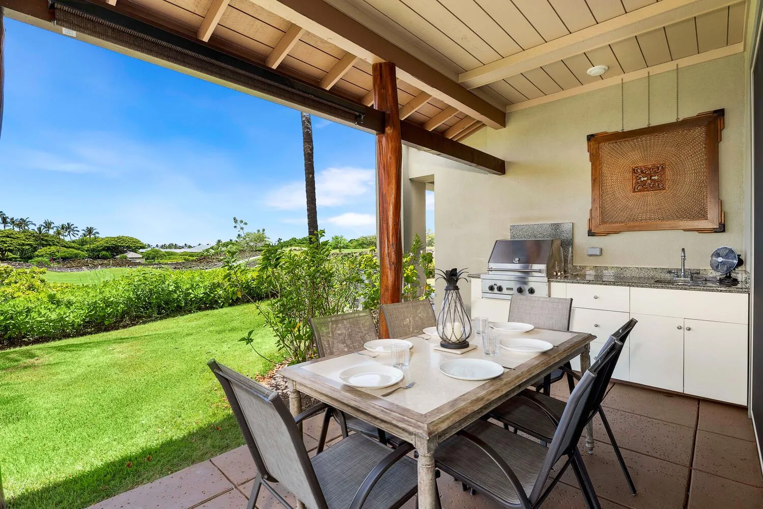 Comedor exterior cubierto con una mesa junto a un jardín y una parrilla empotrada.