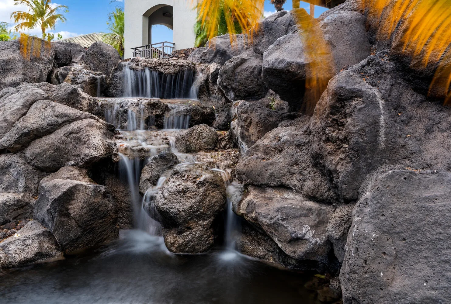 Una cascada entre rocas desemboca en una piscina bajo palmeras.