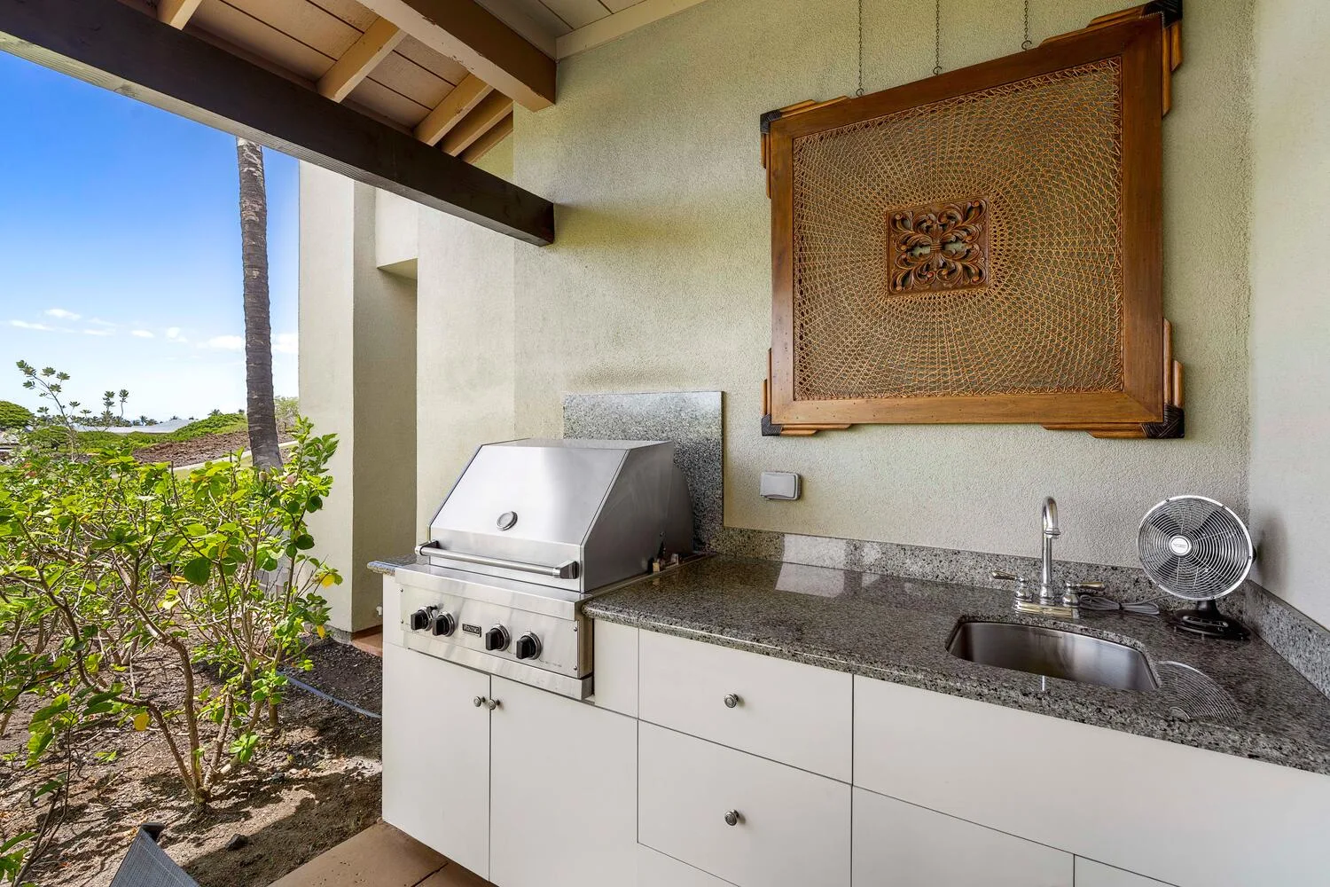 Una encimera de cocina exterior con parrilla, fregadero y vista al jardín.
