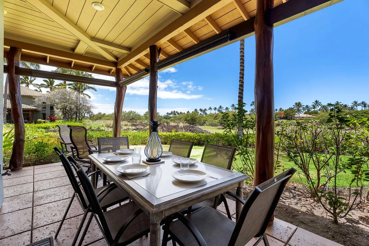 Un comedor exterior cubierto da a un jardín con palmeras.