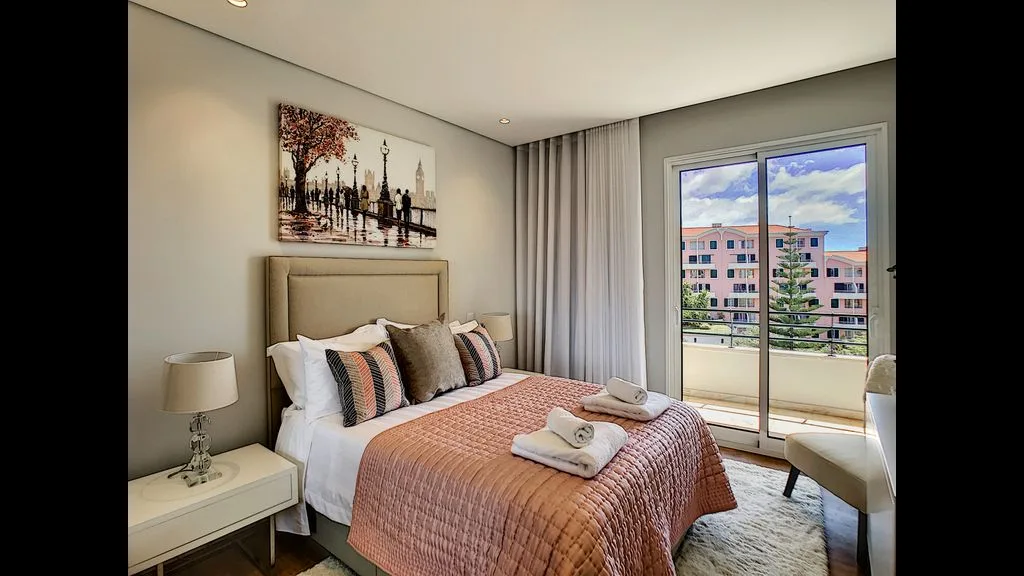 A bedroom with a neatly made bed beside a window and curtains.