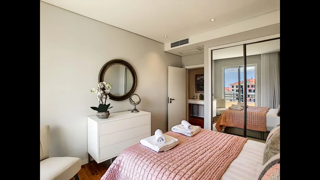 A bedroom with a made bed, dresser, and mirrored closet doors.