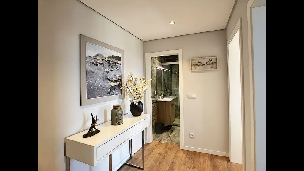 A hallway features a console table, wall art, and an open view into a bathroom.