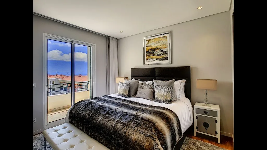 A bedroom with a neatly made bed and sliding glass doors to a balcony.