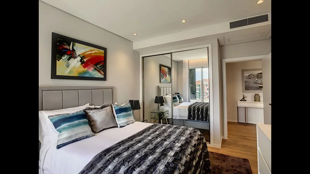 A bedroom with a bed, colorful wall art, and mirrored closet doors.