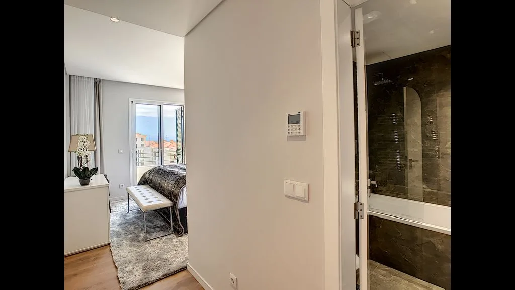 A bedroom opens onto a hallway beside a bathroom with a glass shower.